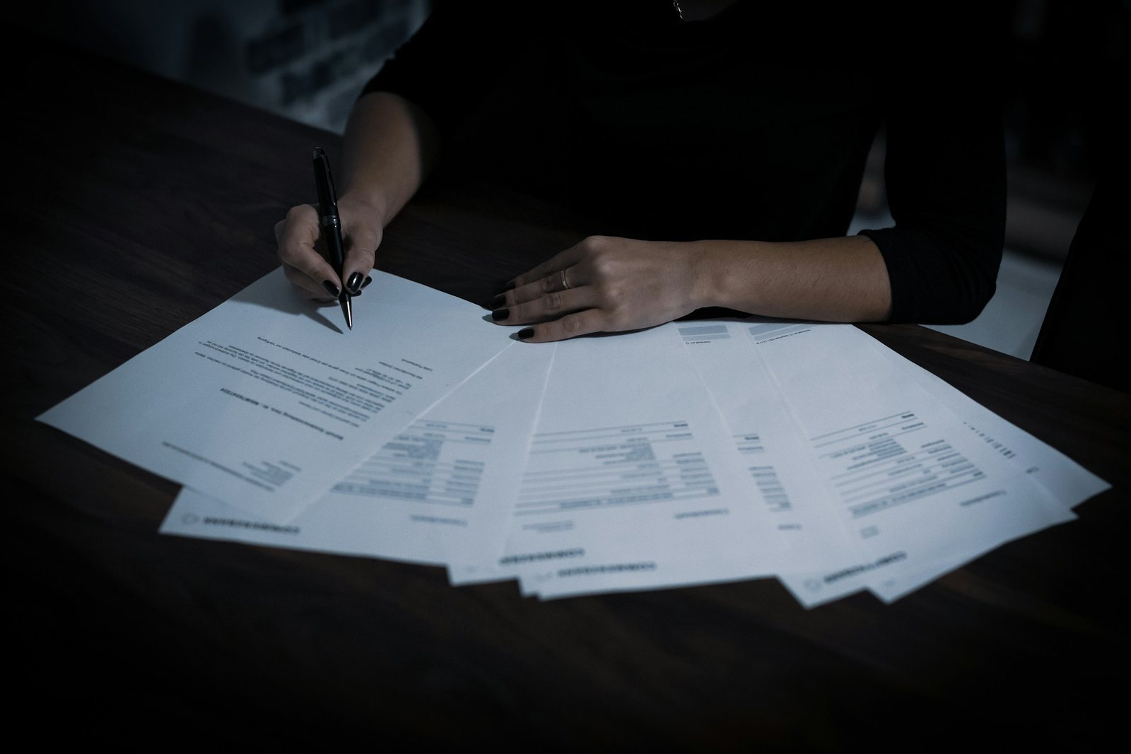 Contract pages spread across a desk, one being signed.