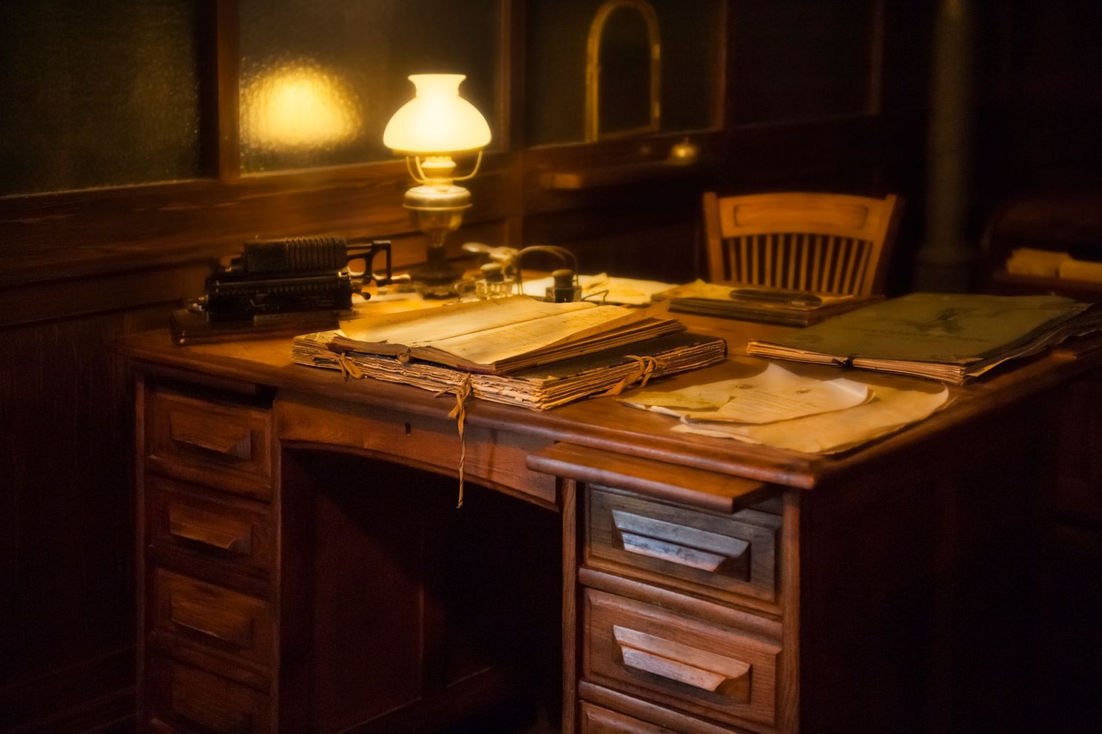 A writing desk and lamp in a private study at dusk.