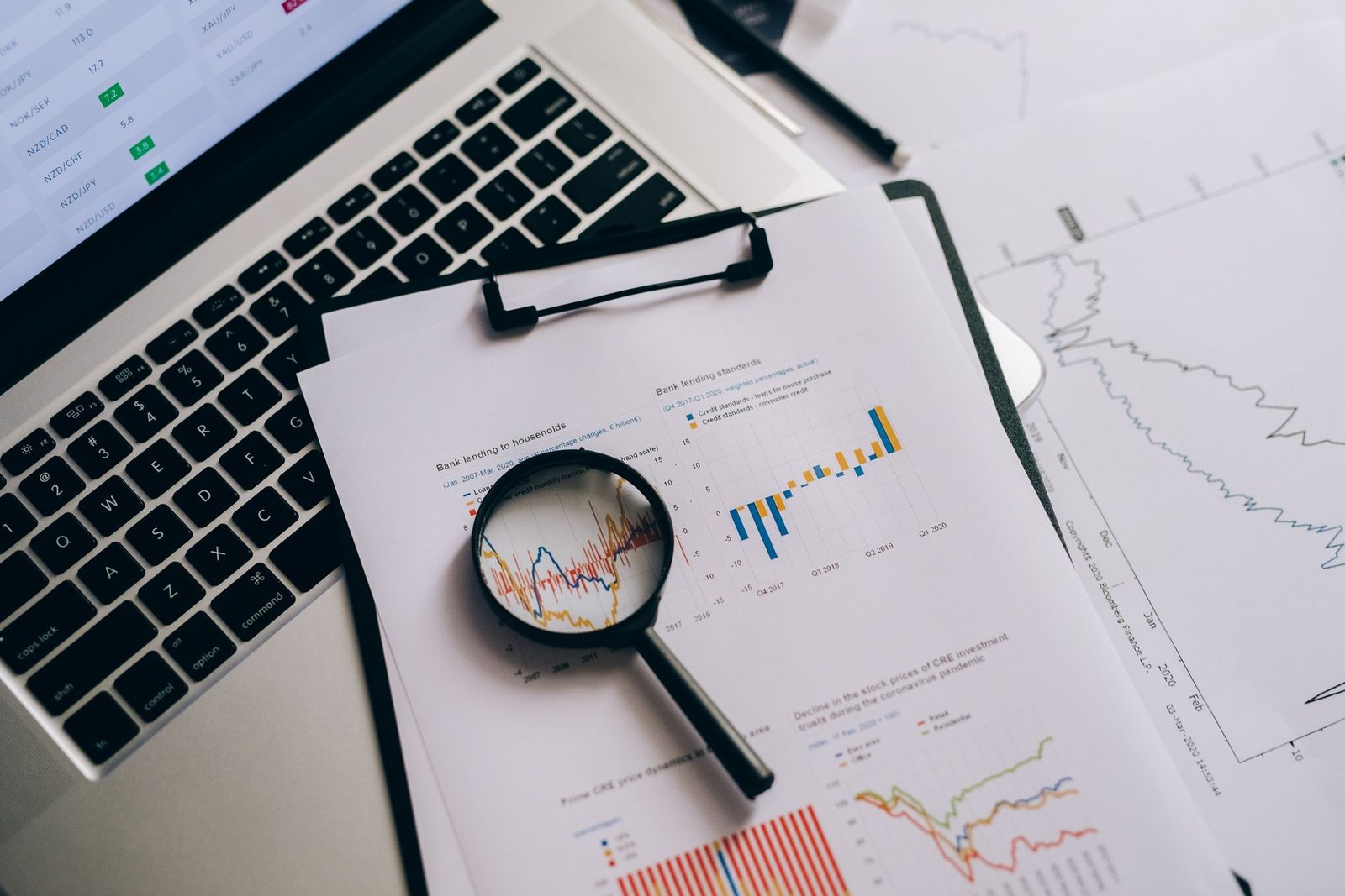 Printed financial charts and a magnifier beside a laptop.